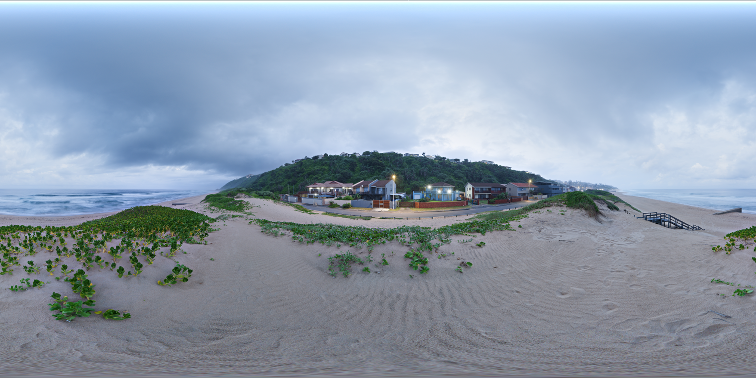 Unclipped, free 24K HDRI of an evening beach: overcast blue hour, soft even light, cool sea and sky, warm street lamps adding gentle highlights.