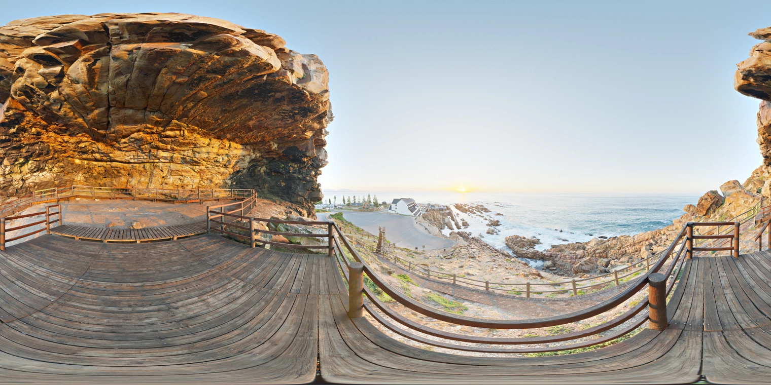 Unclipped, free 24K HDRI of a coastal cave boardwalk at sunset: warm golden light, cool blue sea and sky, soft shadows, crisp detail and wide dynamic range.