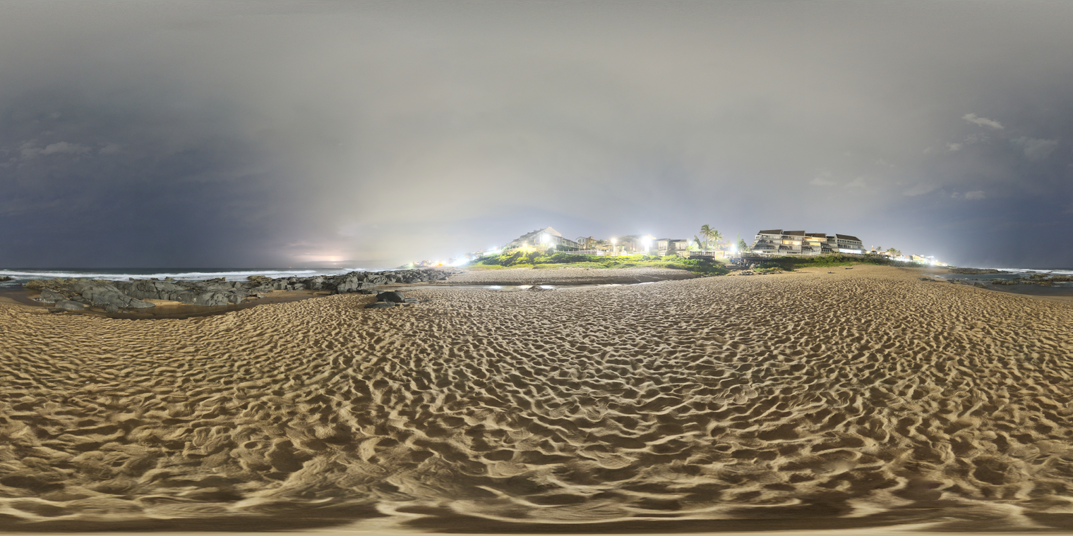 Unclipped, free 24k beach at night with cloudy sky, distant surf, and bright coastal buildings. Cool ambient glow, warm sand, crisp highlights, hard shadows.