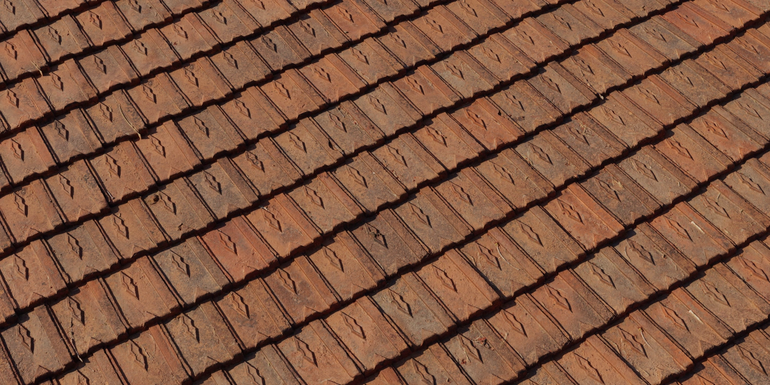 Free 8K clay roof tile texture of weathered, uneven terracotta tiles with overlapping rows, chipped edges, gritty dirt in crevices and embossed diamond shaped details.