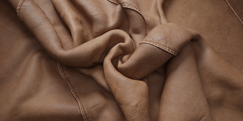 Free 8K texture: aged chestnut leather upholstery with fine grain, visible stitching, creased and wrinkled surface, worn edges, and a soft satin sheen.