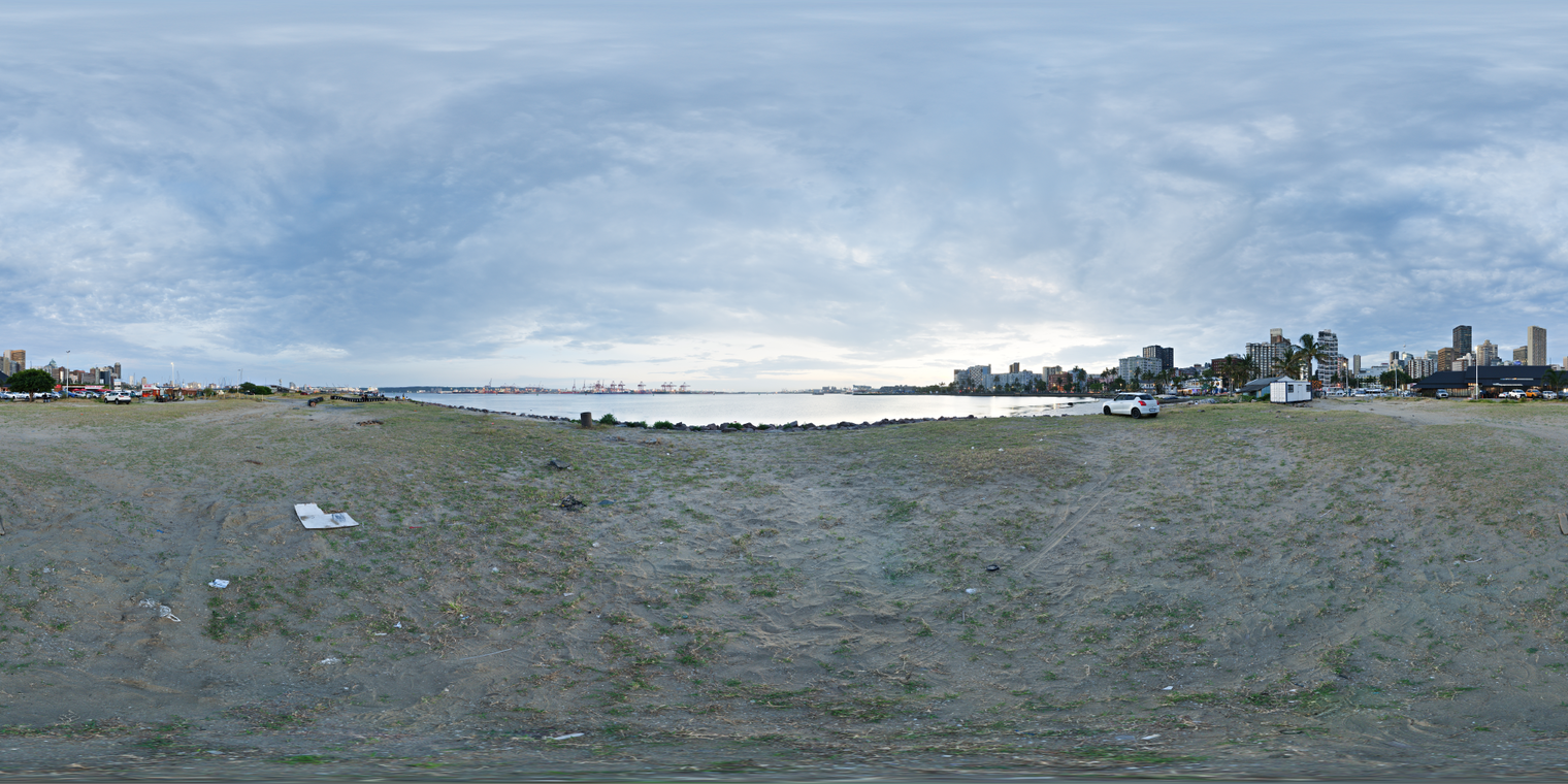 Unclipped, free 24K HDRI of a dusky city beach; heavy clouds, cool blue tones, soft diffuse light, gentle water glints, distant skyline and cranes.