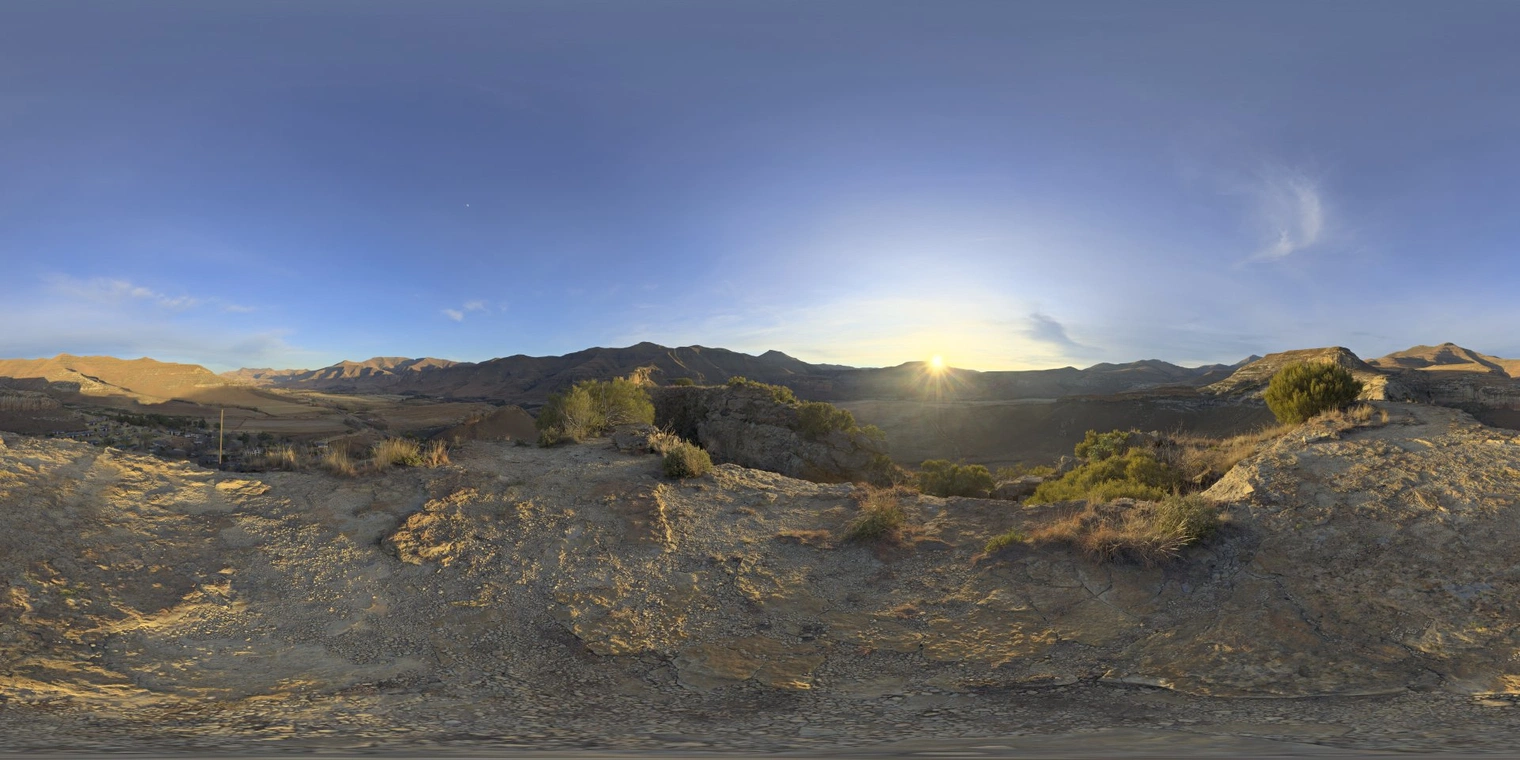 Free 16K unclipped HDRI. Warm sunrise over dry hills and distant mountains, partly cloudy blue sky, strong directional low-angle golden light, high contrast shadows.