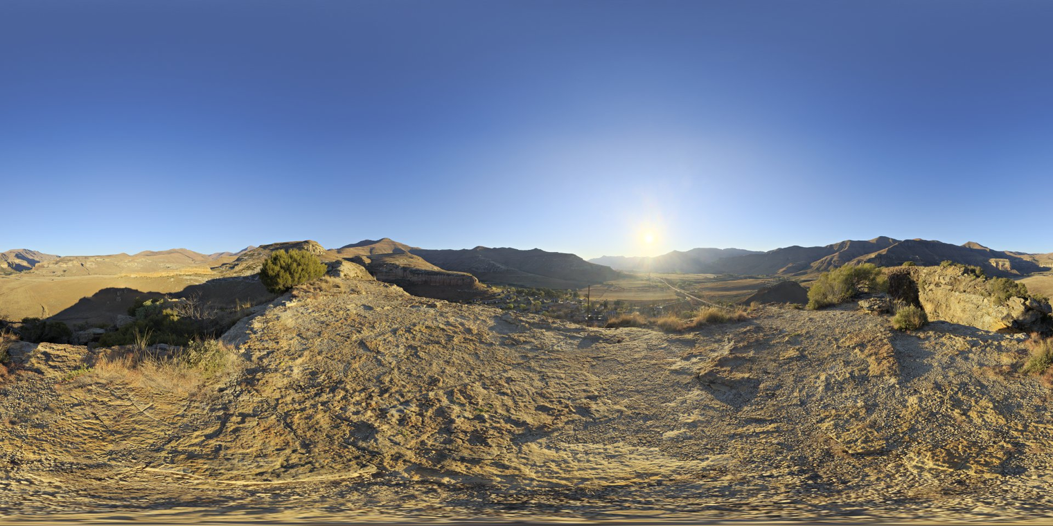 Free 16K unclipped HDRI: late-afternoon sun over rocky mountains and valley, clear blue sky, warm low sun with strong directional, high-contrast natural light.