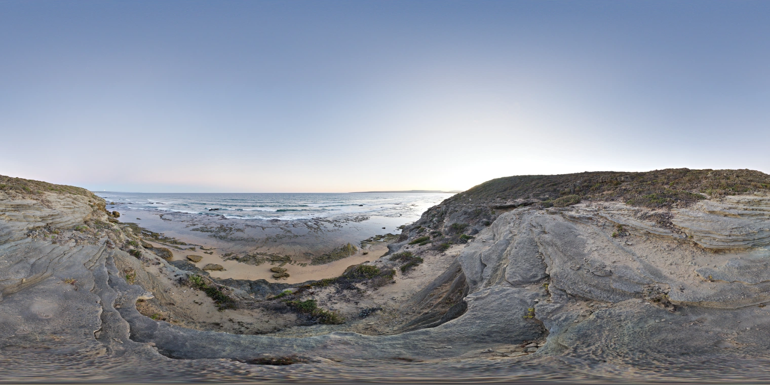 Unclipped, free 24K HDRI capturing a rocky beach overlook at dusk, with soft cool skylight, low sun glow, clear horizon, crisp reflections, and subtle shadows.