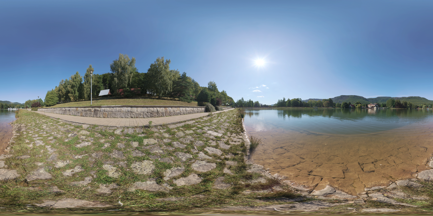 Unclipped, free 29k HDRI: bright midday sun, clear blue sky and high-contrast natural light; calm lake reflections, paved shore and crisp shadows.