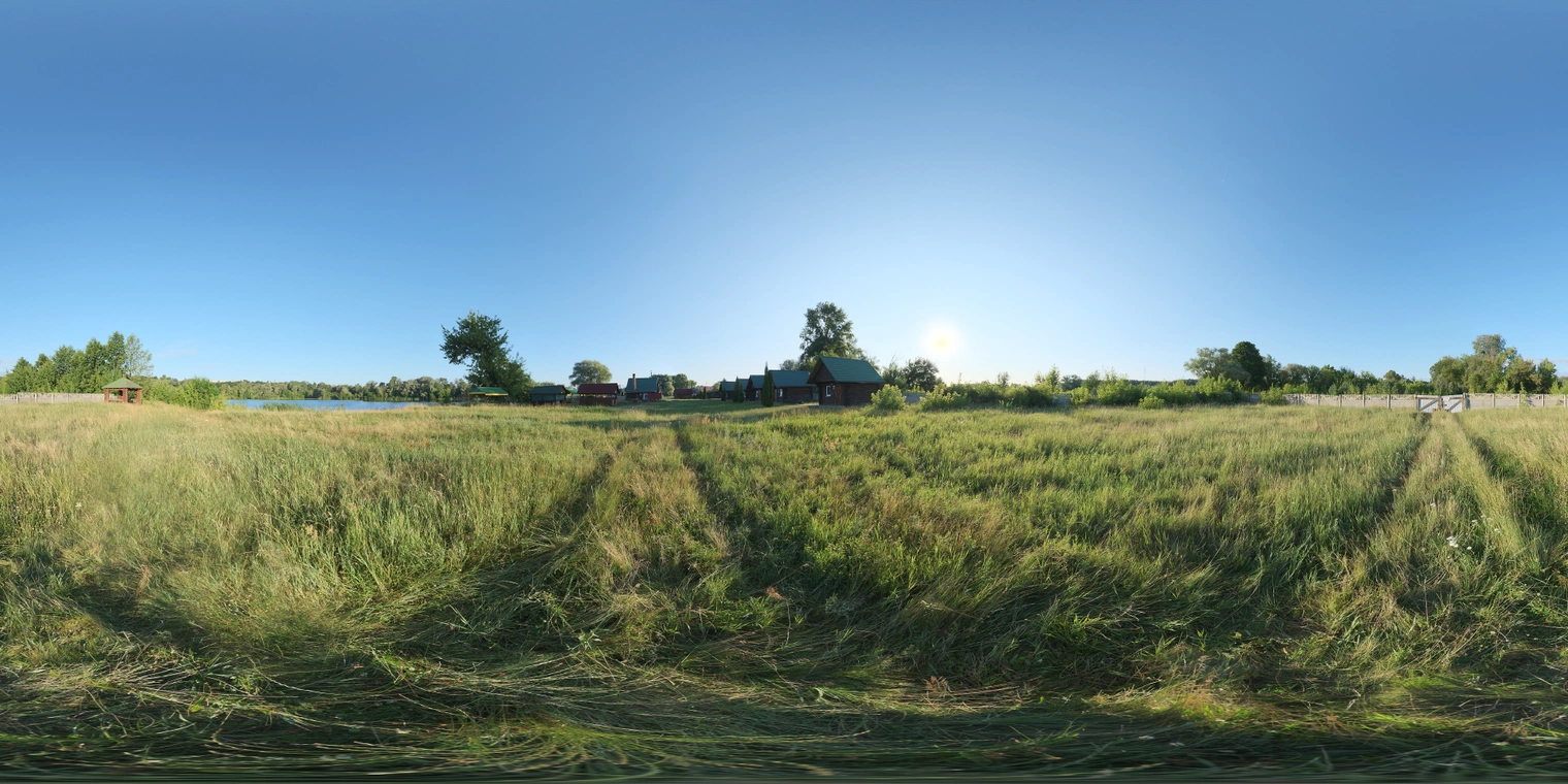 Unclipped, free 16K HDRI of a sunlit field - clear blue sky, warm low sun, high-contrast shadows across long grass, trees and cabins, serene morning/afternoon mood.