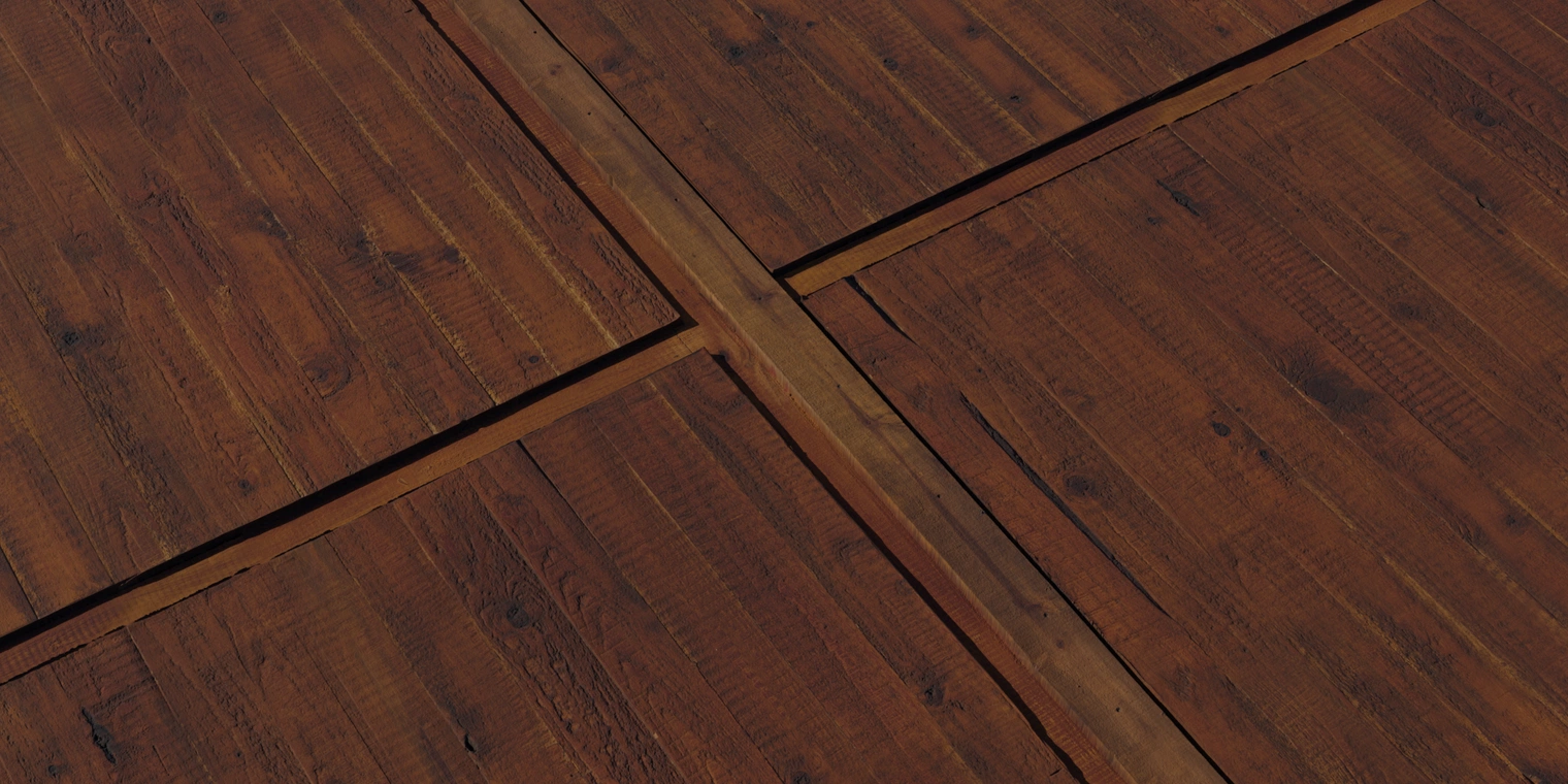 Free 8k texture of a weathered rough-hewn pine door: deep reddish-brown planks, pronounced grain, split edges, nail holes and a worn matte finish.