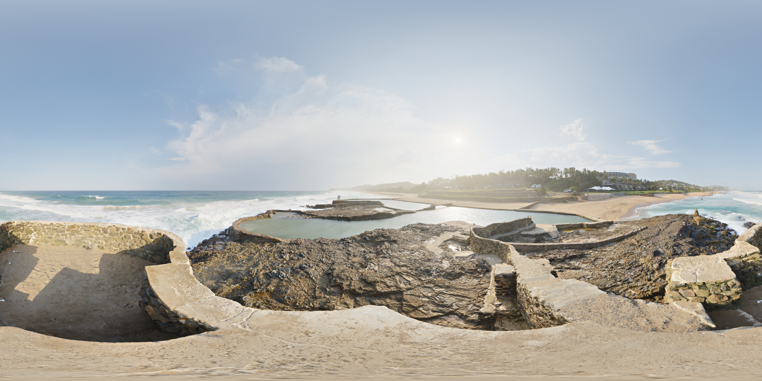 Unclipped, free 24K HDRI of a sunny tidal pool on rocky coast, bright low sun with thick haze, crisp shadows, cool blue sky, warm stone and sparkling surf.