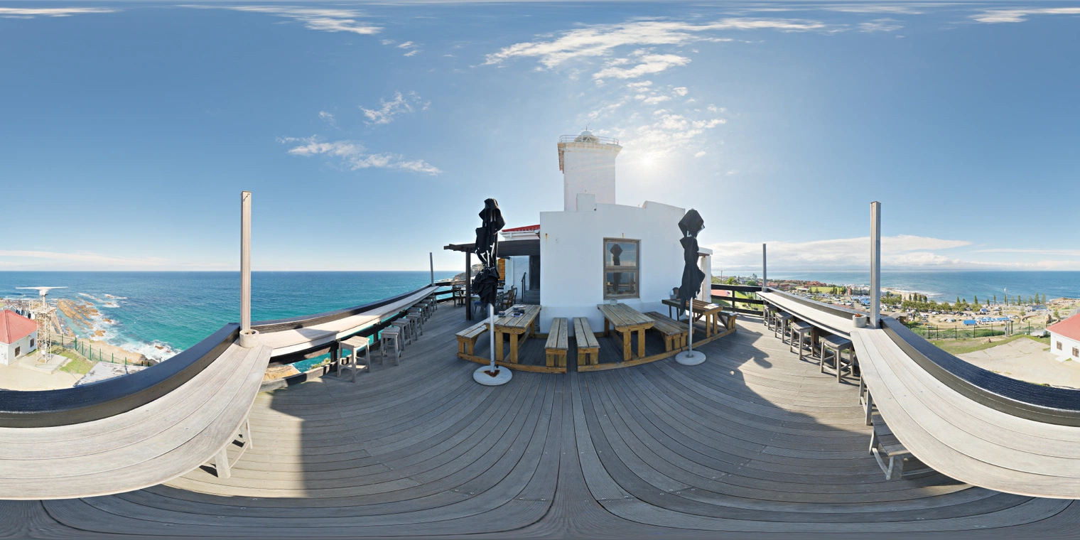 Unclipped, free 24K HDRI of a coastal cafe terrace in bright midday sun; clear blue sky, shimmering sea, hard shadows, warm wood, crisp airy mood.