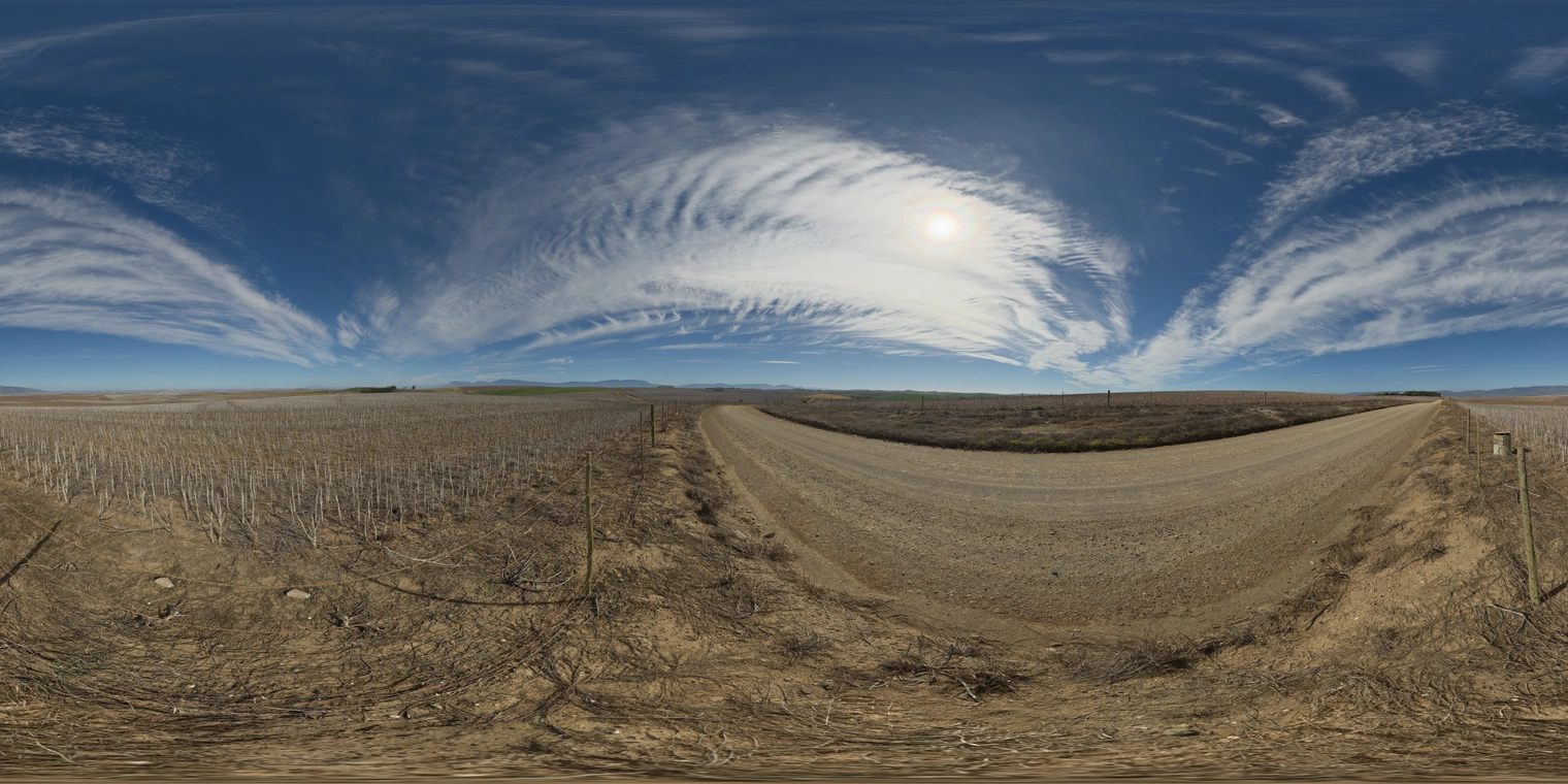 Unclipped, free 24K HDRI of a sunny farm road between dry fields under sweeping cirrus clouds. Bright blue sky, sharp shadows, warm earth tones.
