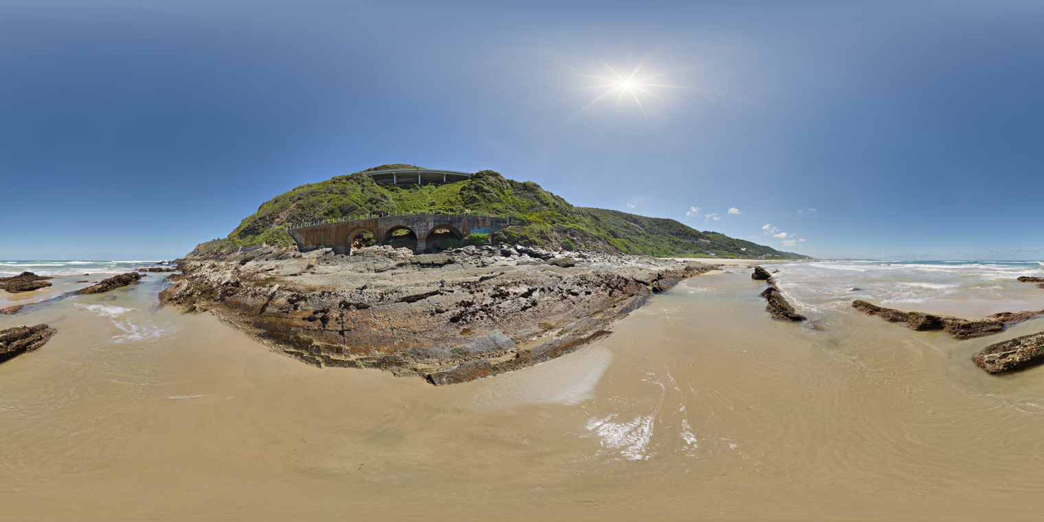 Unclipped, free 24K HDRI with a bright midday sun over a rocky beach; clear blue skies, warm sand, wet tide pools, crisp highlights and punchy shadows.