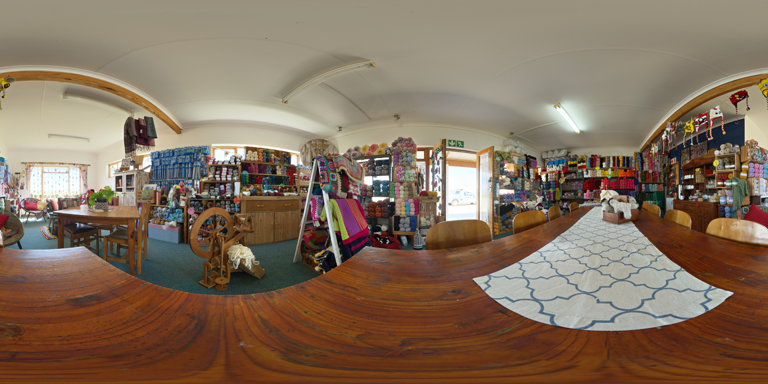 Unclipped, free 24K HDRI of a cozy wool shop interior with warm mixed lighting - fluorescents and window daylight - soft shadows, colorful shelves, wooden tables.